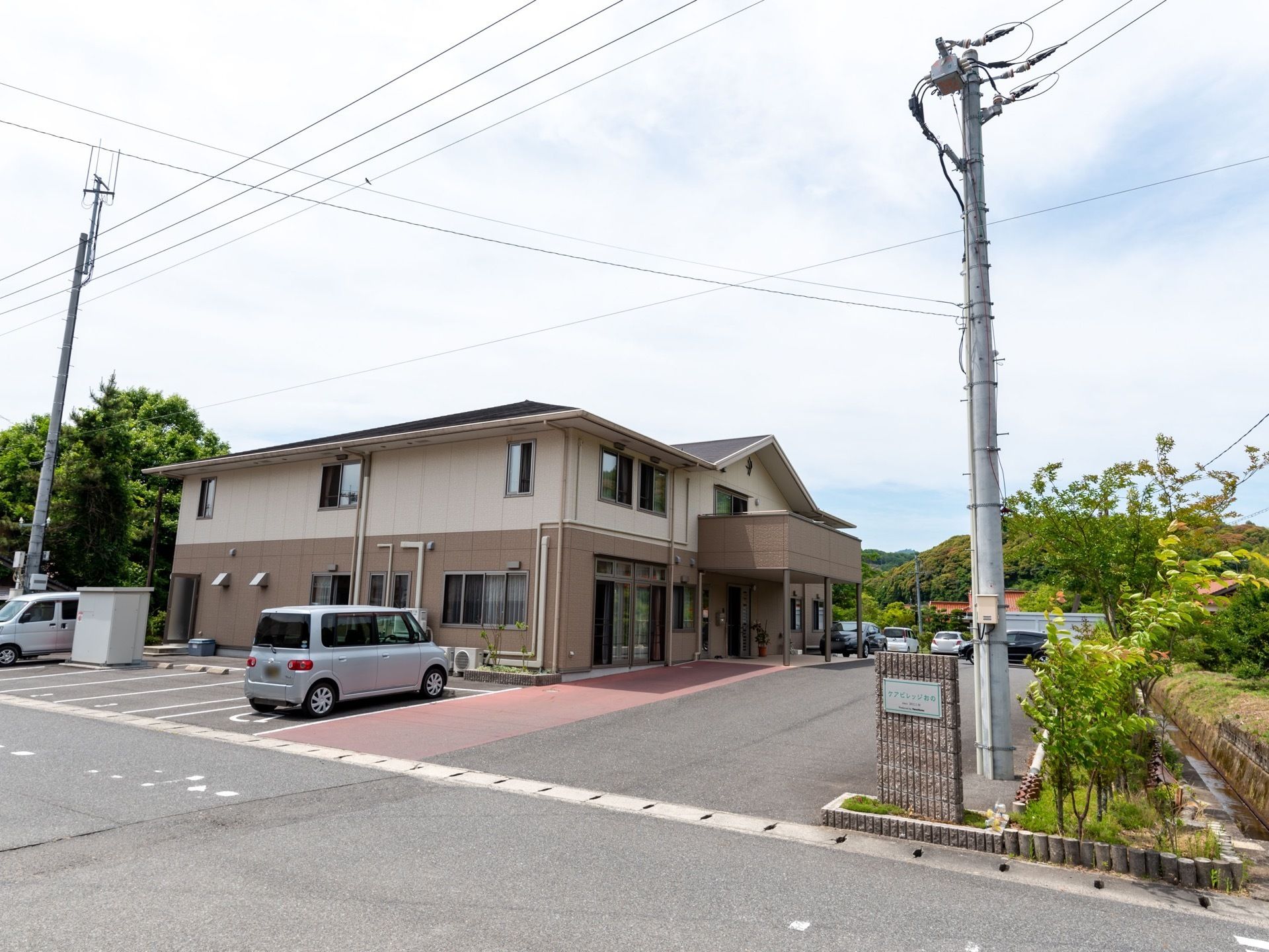 施設は２階建ての建物で、周囲には緑が多く見られる。道路側に駐車スペースがいくつかある。敷地の入口に施設名を表示したプレートが貼られている。