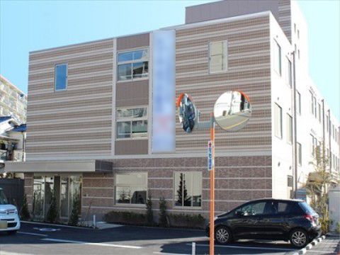 茶色のツートンカラーの横じまの外壁で、手前が駐車場になった3階建ての建物