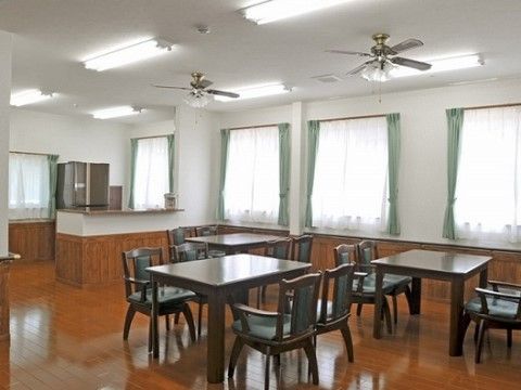 カウンターキッチンが備え付けられたリビングで、冷蔵庫が置かれている。ダイニングテーブルのセットが複数組セットされている。