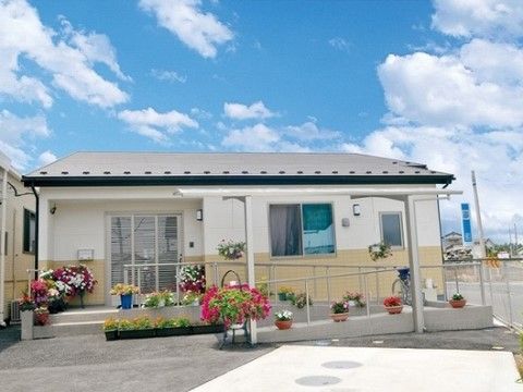 玄関前に階段や手すりのついたスロープが設置されており、色とりどりの花が植えられた鉢植えやプランターが並んでいる。