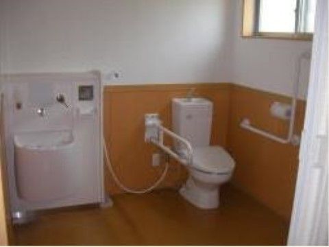温水洗浄便座付きの便器と手洗いが横並びに設置された広いトイレ。壁には窓があり、手すりが付いている。床はバリアフリーになっている。