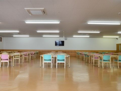 天井が高く広いスペースの中に、テーブルと手すり付きの椅子が数多く置かれている。壁には手すりが設けられ、テレビが設置されている。