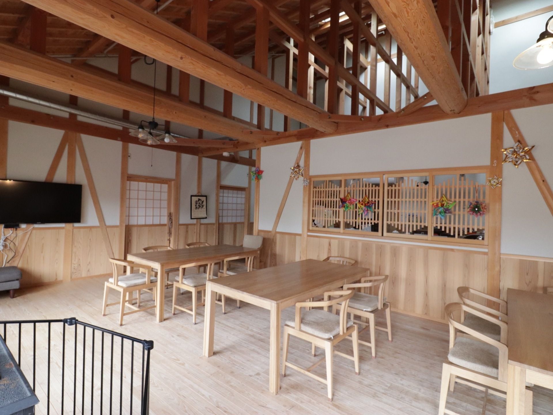 天然の木材で作られたテーブルや椅子が並んでいる。それぞれの椅子には白い座布団がおかれている。壁掛けテレビや薪ストーブがある。