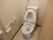 アイボリーの床と壁でまとめたトイレスペース。温水洗浄機能の付いたトイレがある。立ち上がるときに便利な手すりがついている。