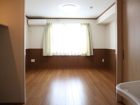 こげ茶のフローリングの床からつながるように白い壁半分まで同系色の木目調でまとめた室内。窓から自然光が入り込む。エアコンも完備している。