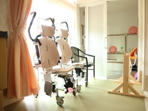 ピンクのカーテンがある窓の前に置かれている、2台のピンク色の入浴用車椅子