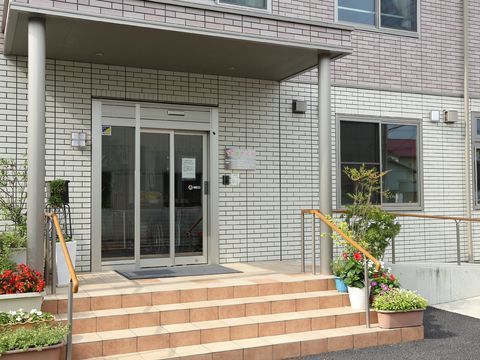ベージュ系のツートンカラーのタイル張り風の外壁にオレンジの階段のある玄関