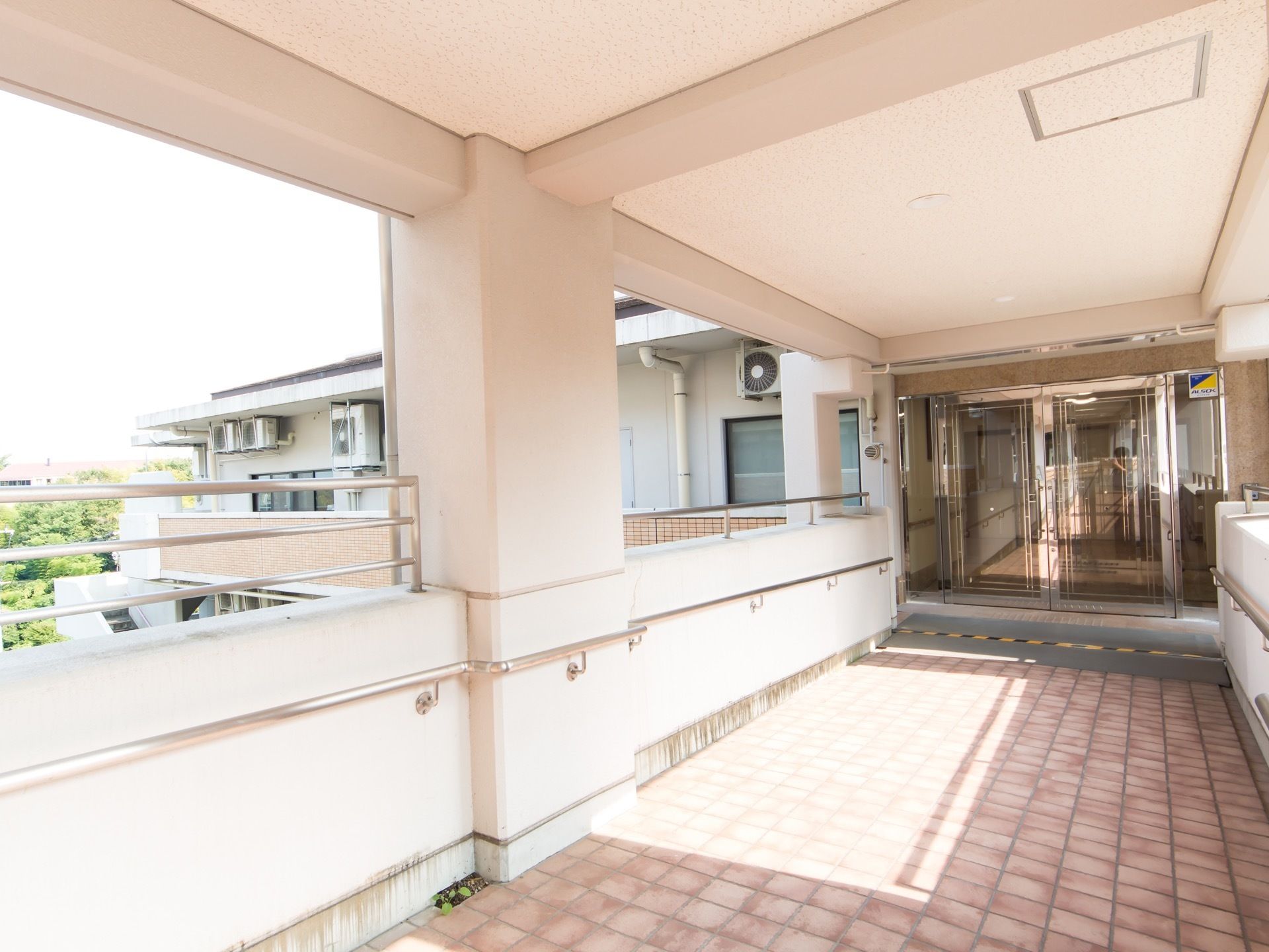 建物の３階部分にある玄関。玄関先は立体通路になっており、上部分は天井に覆われている。ガラス張りの両開きの自動ドアが付いている。