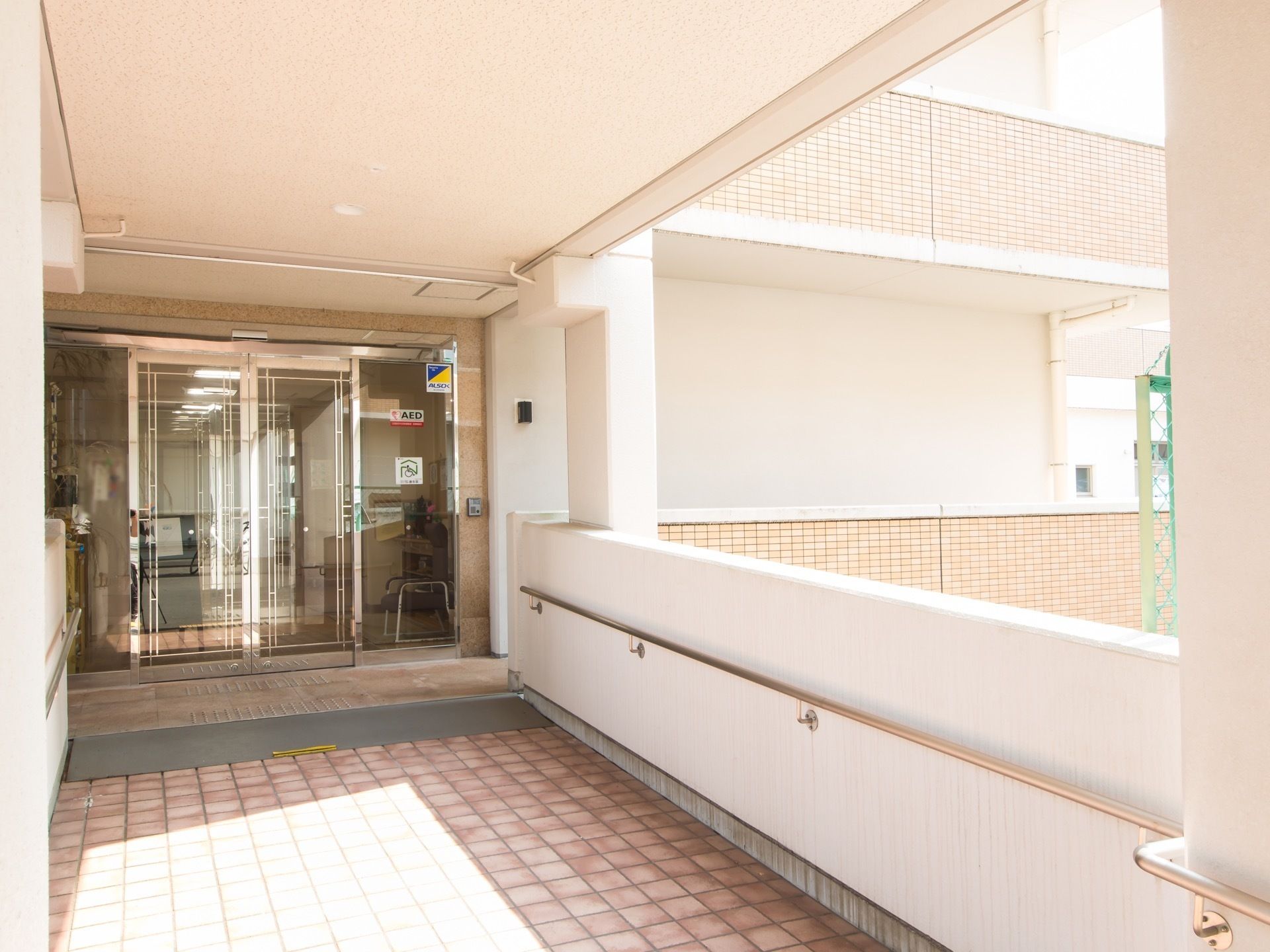 建物の３階部分にある玄関。ガラス張りの自動ドアがある。玄関前の通路は立体通路があり、低い壁と天井で囲まれている。