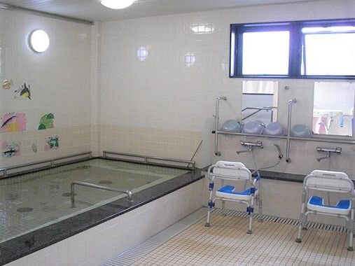高い位置に窓があり、浴槽には手すり、シャワー前にはシャワーチェアが設置された浴室
