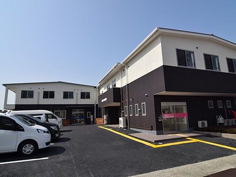 大きな駐車スペースの奥に、黒と白のスッキリとした2階建て建物
