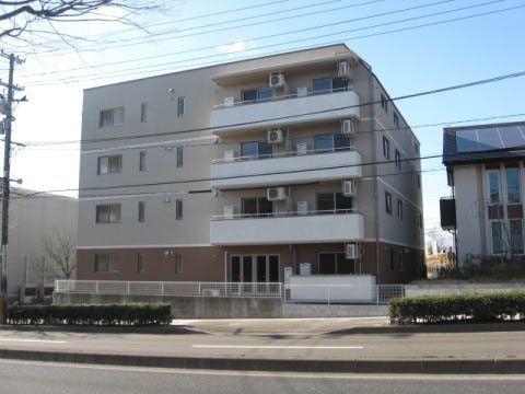 1階だけブラウンに塗られた、ベージュ色の4階建ての建物
