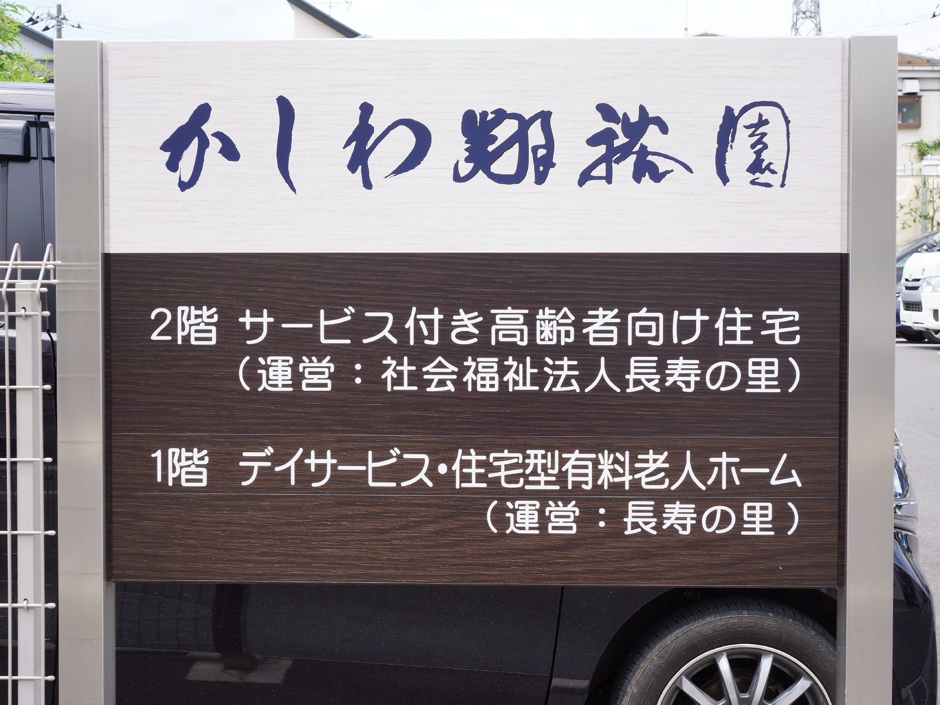 施設の玄関前には、白地に黒い筆文字で施設名が書かれた看板が掲げられている。その下にはサービス内容が書かれている。