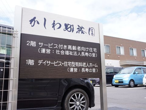 建物とその前に広がる駐車場の手前に建てられた白とブラウンの看板