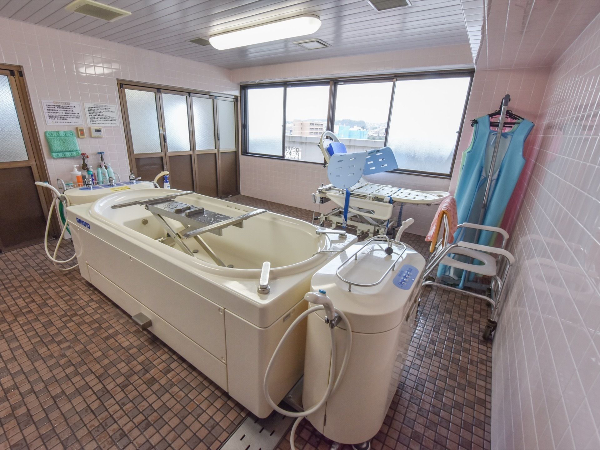 浴室にはタイル式の床が一面に敷き詰められており、浴槽は補助器具付きとなっていて、奥に入居者様を乗せる担架がある。