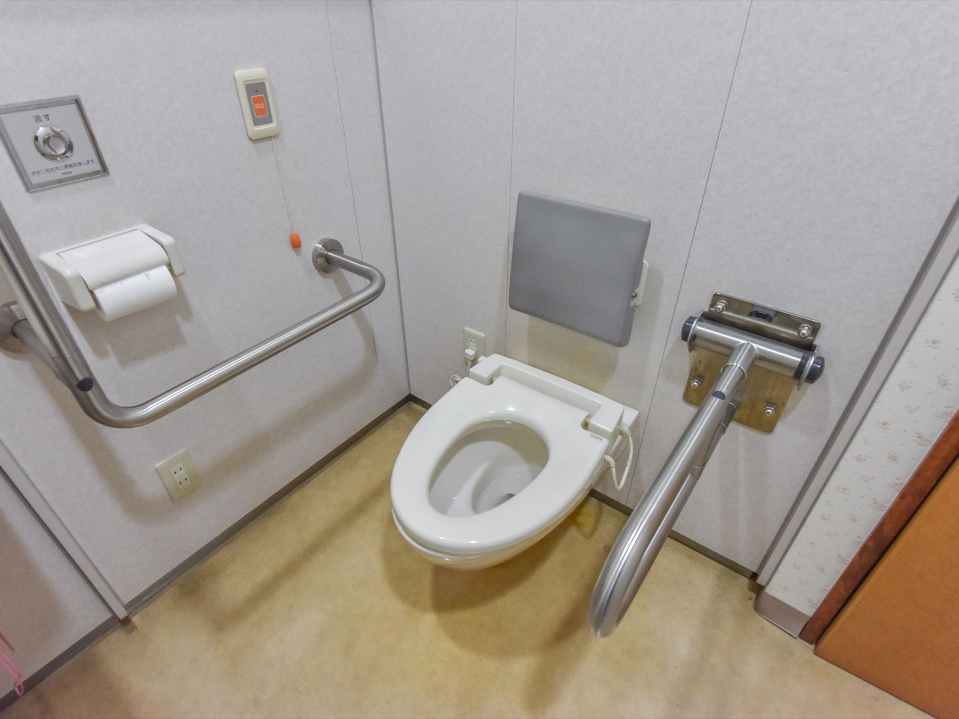 トイレにある便座は蓋の無いタイプになっている。両サイドには手すりがあり、正方形の背もたれも設置されている。