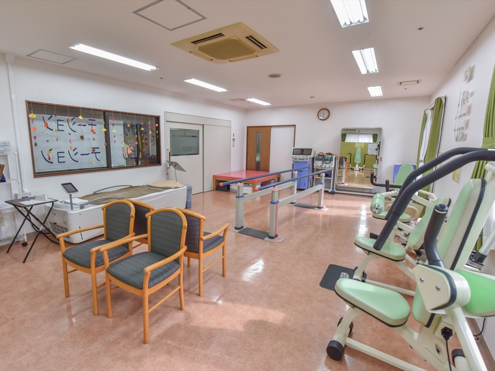 機能訓練室には４つのイスが背中合わせで置かれている他、ベッドをはじめとしてリハビリ用の各種器具が置かれている。