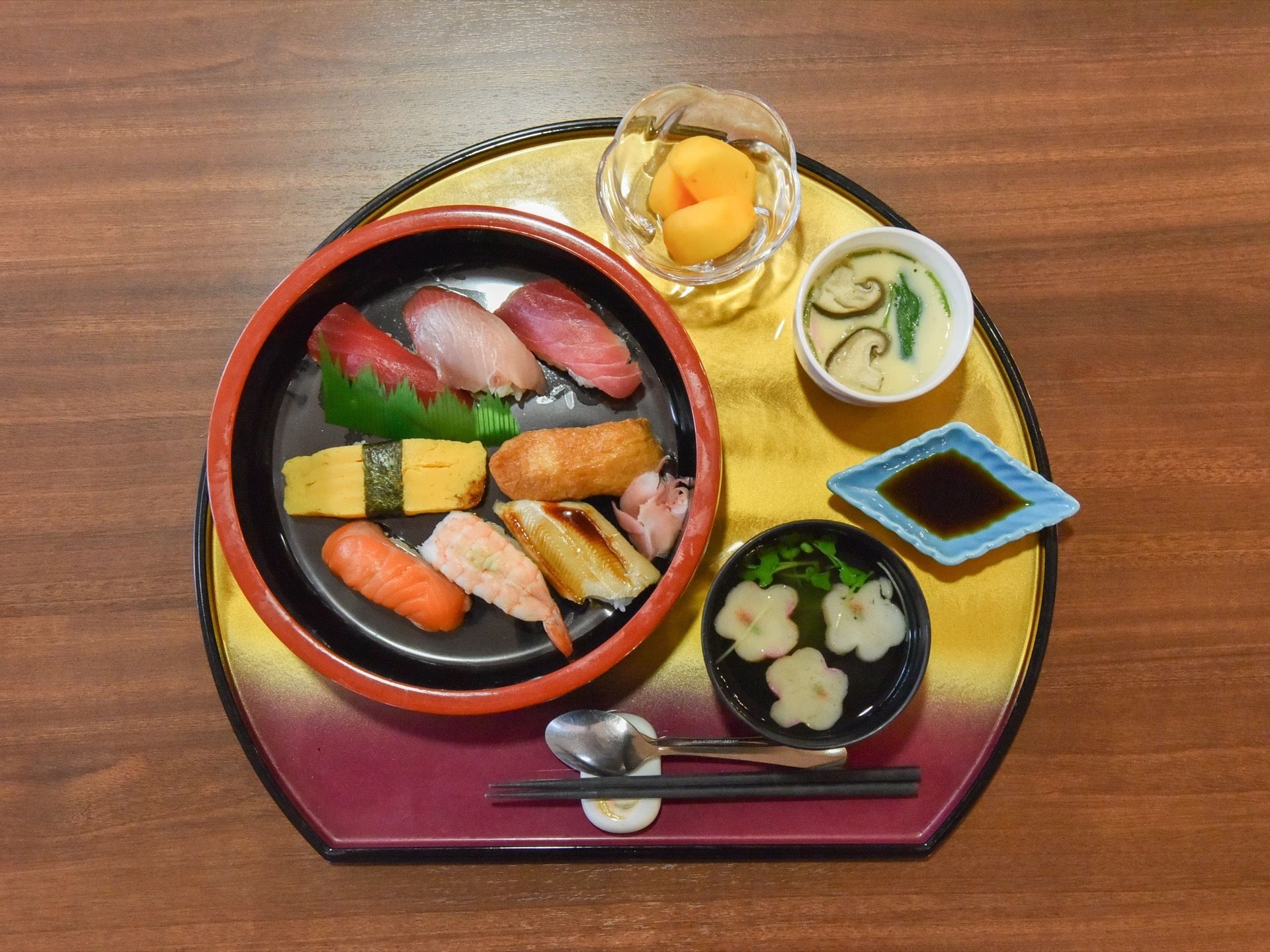 食事が写っている。寿司を中心に、しょうゆ皿、お吸い物や茶わん蒸し、デザートが扇形のお盆の上にのっている。