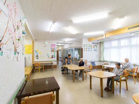 多目的なスペースで、テーブル椅子が置いてあり、入居者が数名安らいでいる。壁には、折り紙などで作られた様々な工作が貼ってある。