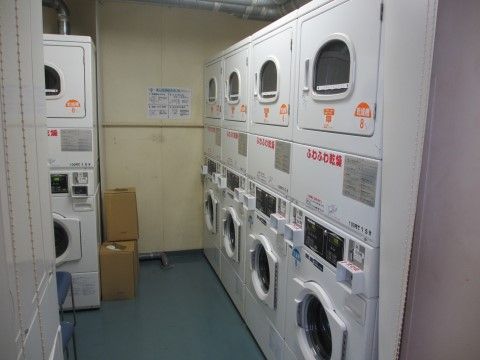 ドラム式の洗濯機とふわふわ乾燥ができる乾燥機がそれぞれ５つずつ設置されている。洗濯機の横に段ボール箱が重ねて置かれている。