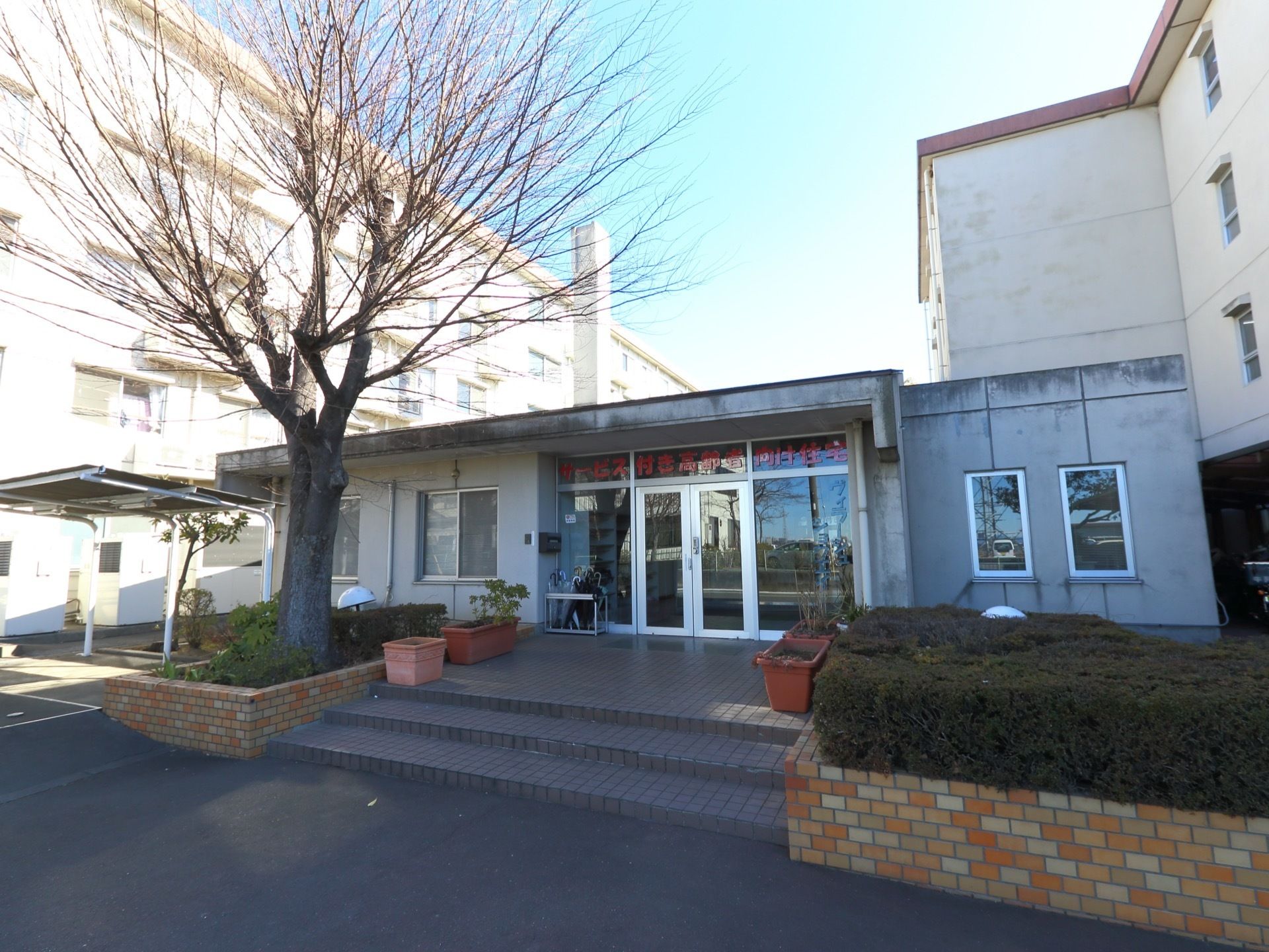 大きな木が傍らに植えられ、緩やかな階段を登った先に、ガラス戸の入口がある。入口の傍らには、自転車置き場も併設されている。