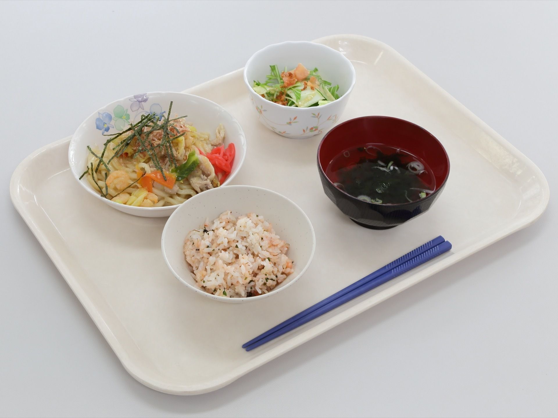 お盆に乗せられた、３品とごはん。野菜サラダ、わかめスープ、野菜と肉の焼うどん、雑穀ご飯の栄養バランスのいい献立。