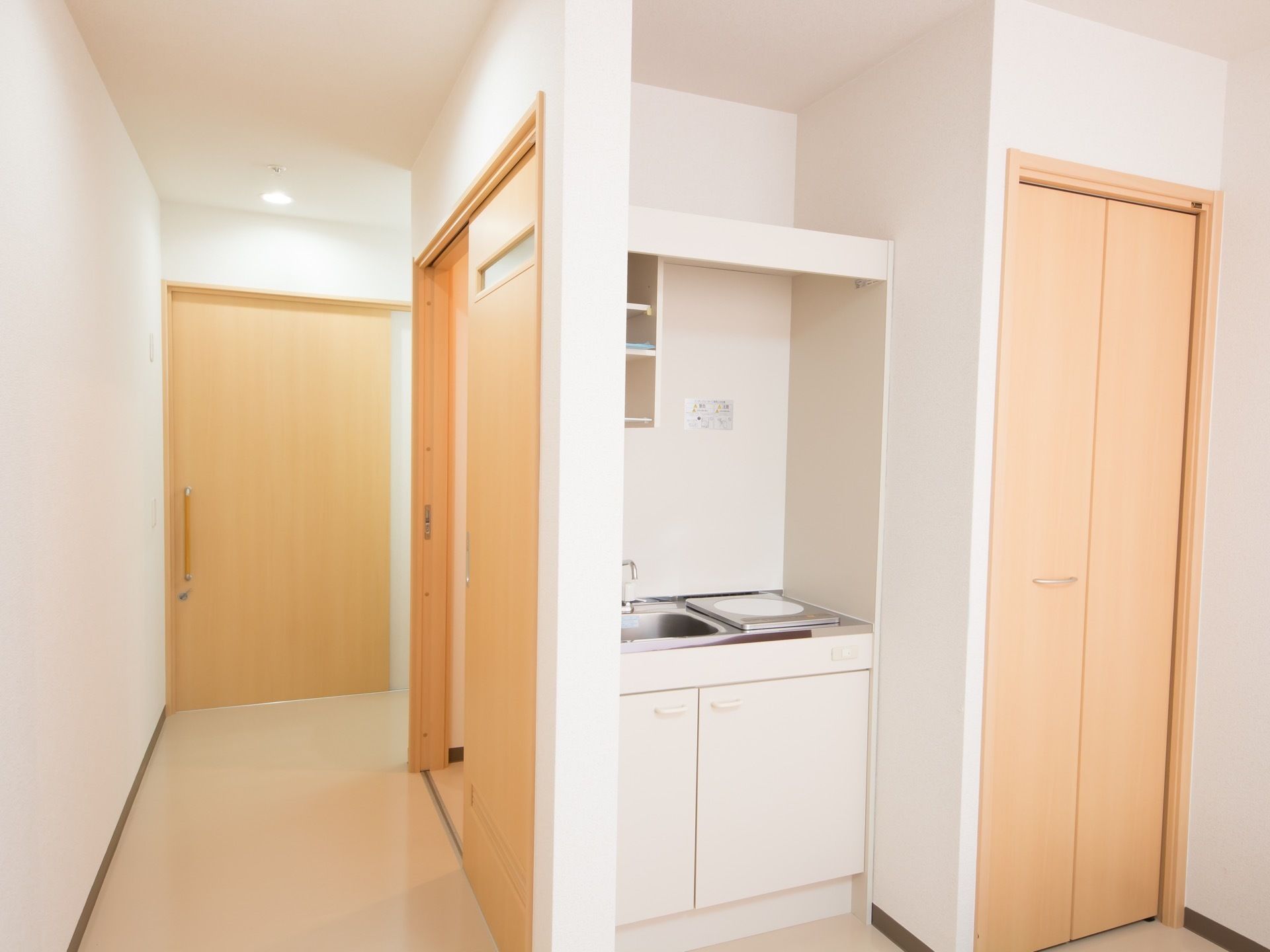電気コンロと小さなシンクのミニキッチンの横にクローゼットが設置されている。トイレのスライドドアが開けられている。