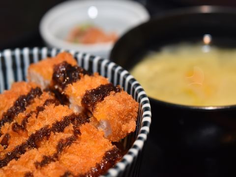 ソースのかかったカツが盛られた縞模様の皿と味噌汁、小鉢が添えられた食事例