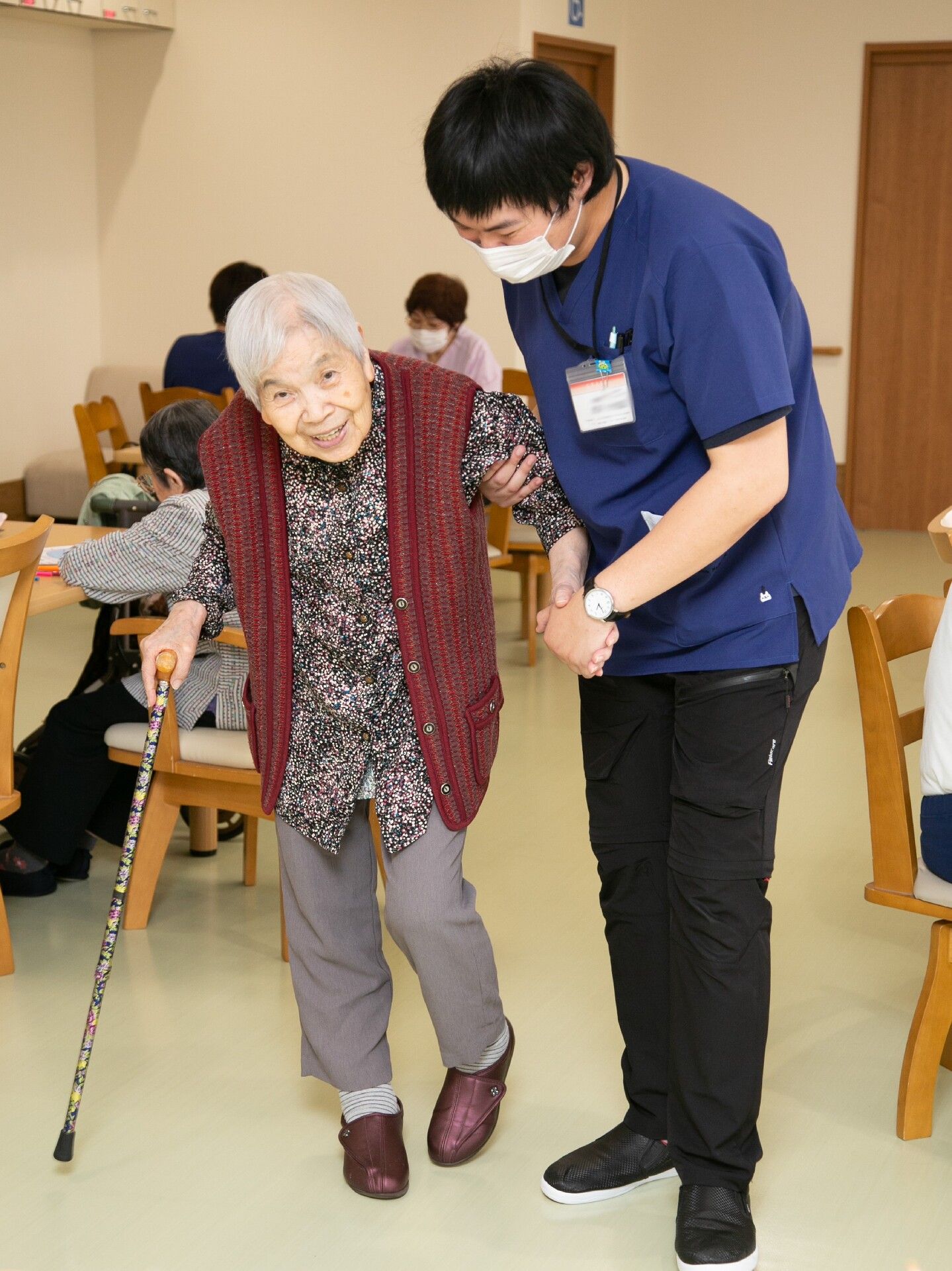 杖を突いて歩く高齢女性を介助する男性スタッフ