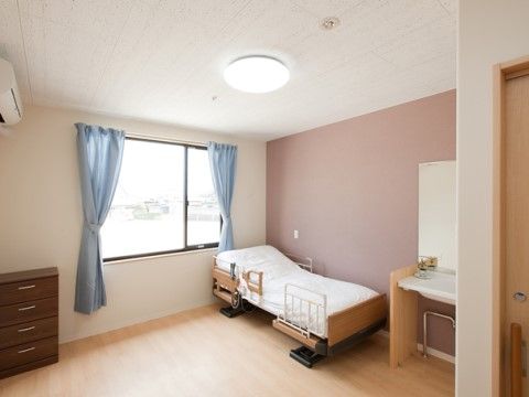 リクライニングベットが設置された高齢者用の居室。エアコンが設置されたフローリングの洋室。