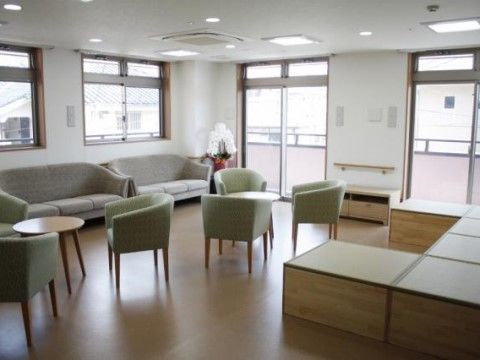 2面に窓があり、左の窓際にカウチソファが2つ、丸テーブルに3つ椅子を置いたものが2セットあるスペース