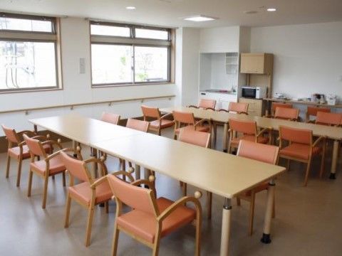左に2つの窓、奥にミニキッチンのある、テーブルの並べられた食堂