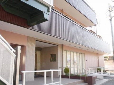 茶色い縦ストライプのベランダが2、3階に見える、白い手すりの付いた玄関