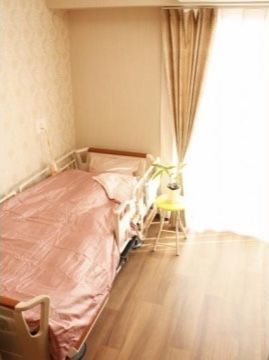 ベージュのカーテンがかかった窓の左側に置かれているピンクのカバーの付いたベッド