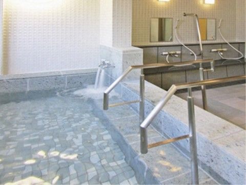 グレーの石造り風の浴槽に手すりが付けられ、奥にシャワーが見える浴室