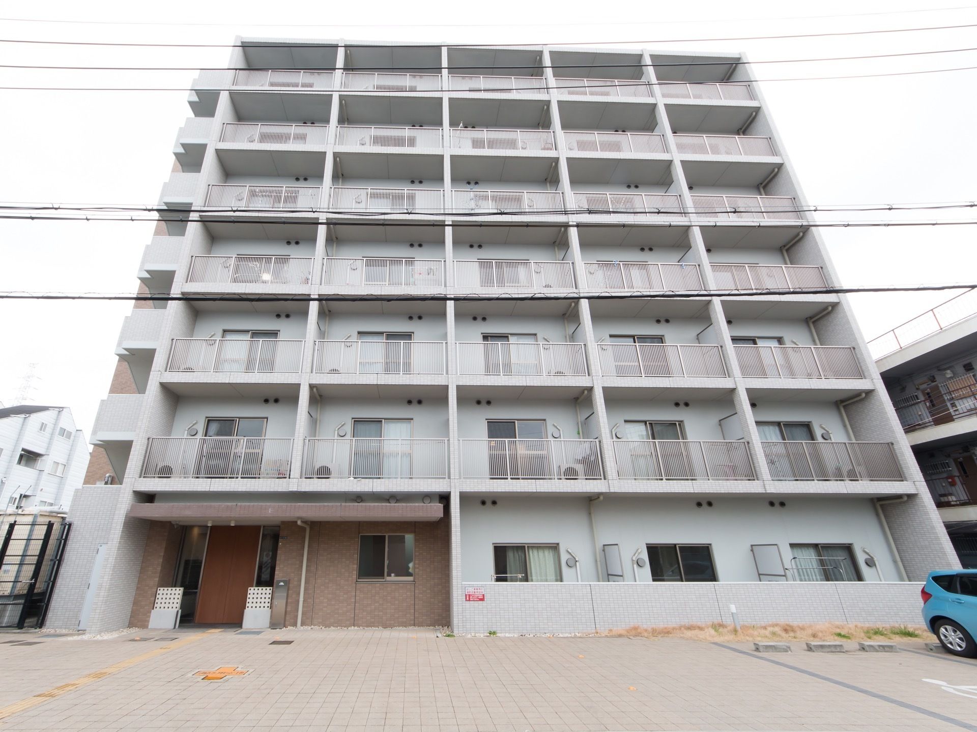 7階建てのマンションのような外観である。ベランダに面した大きな窓には網戸が備わっている。玄関の前には駐車スペースがある。