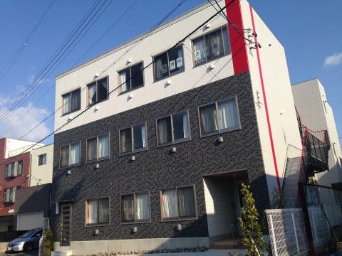 1、2階は濃いグレー、3階は白に切り替えられた、右下に玄関のある3階建ての建物