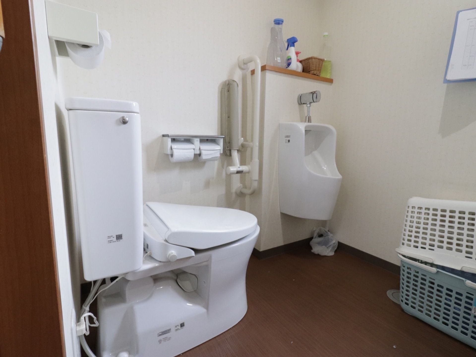 白い便座器や男性用小便器が完備されたトイレである。双方の間には、可動式手すりが設置されており、スペース移動が安全でスムーズである。