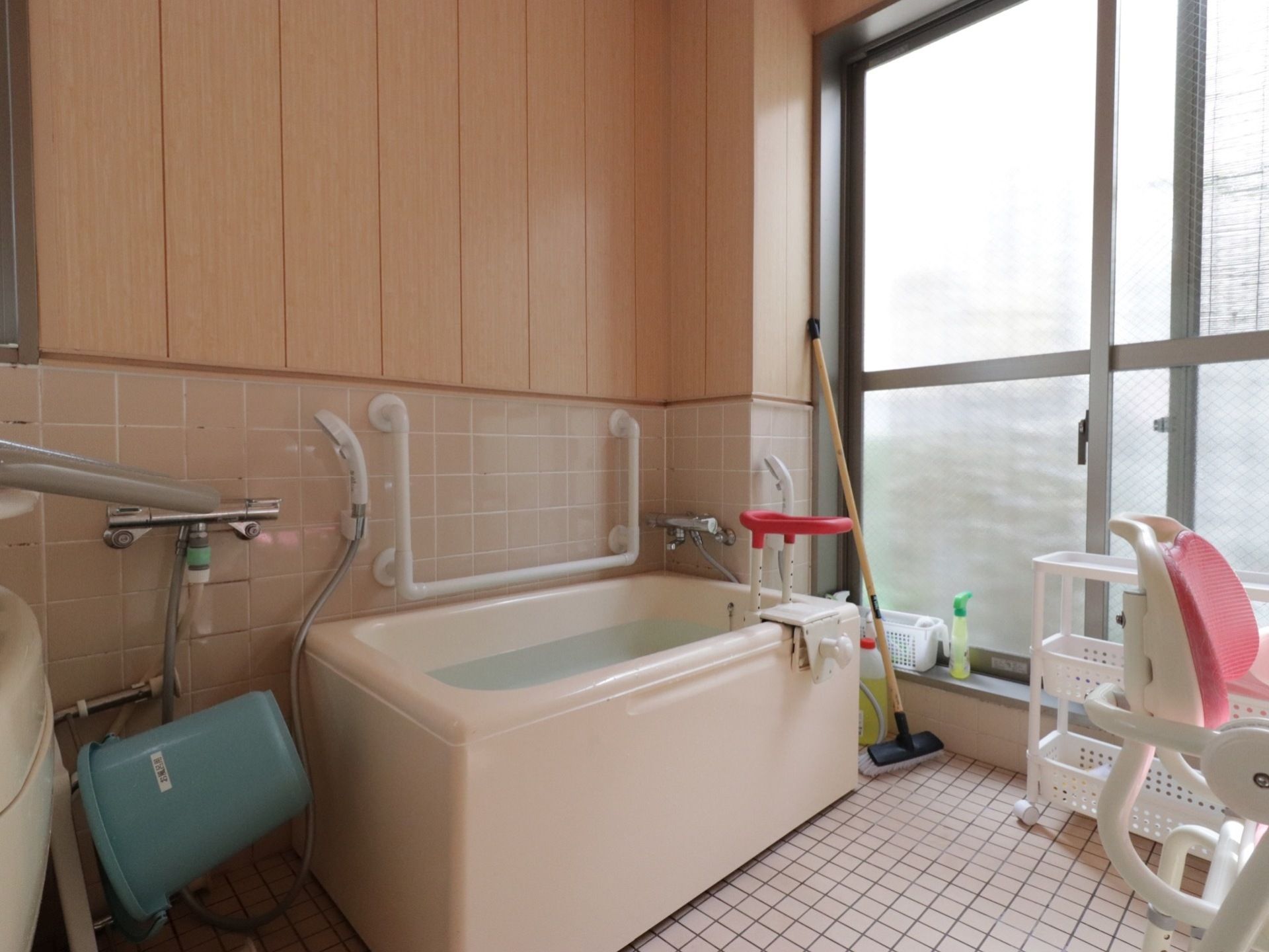 個別浴槽には、湯が張られ入浴介助器具が設置されている。壁にはコの字の手すりが取り付けられ、洗い場にはバスチェアーが置かれている。