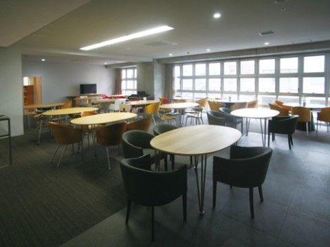 右に格子上の窓があり、丸テーブルに椅子が置かれたセットが並ぶ共用スペース