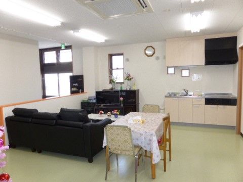 ソファーや椅子、テーブルといった家具が置かれている部屋に、キッチンも設置されている。テーブルには花が添えられている。