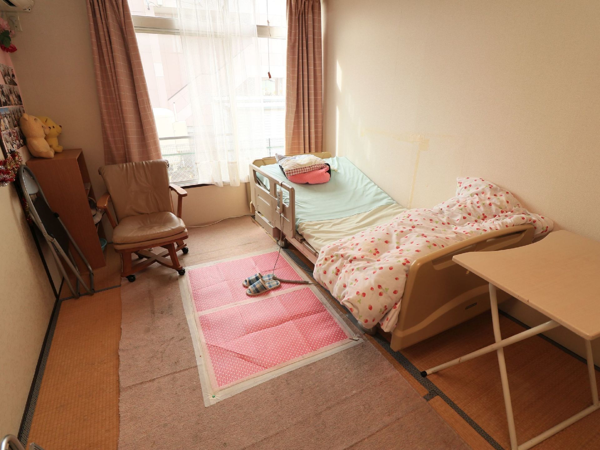 畳敷きの部屋である。介護用ベッドが窓下に置かれ、手前に折りたたみテーブルがある。窓際に整理棚があり、上にぬいぐるみが置かれている。