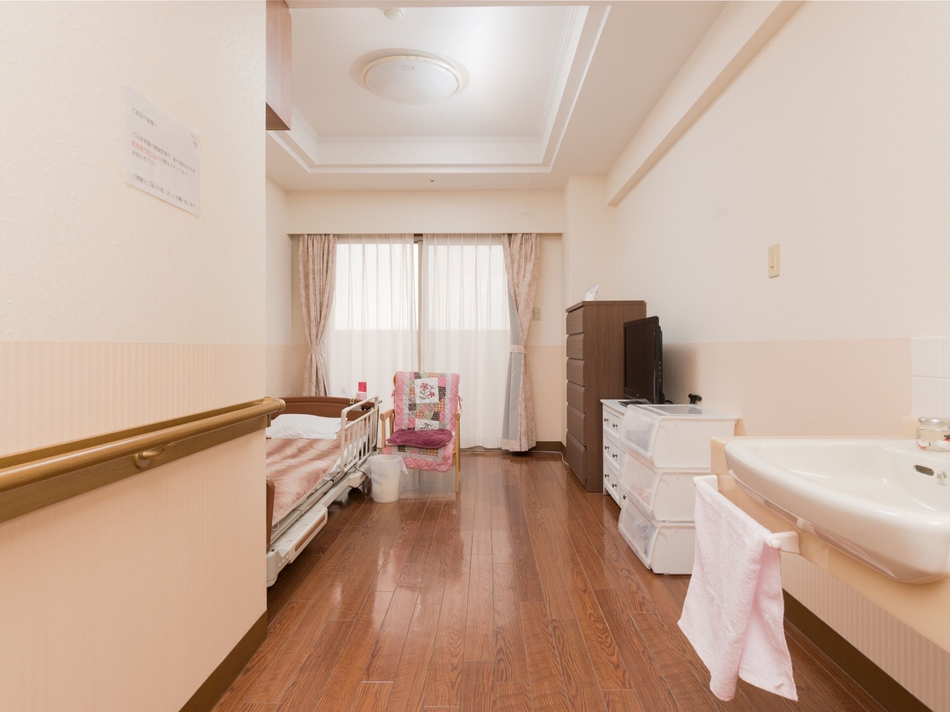 天井が高く、奥行きのある部屋になっている。壁には手すりがあり、洗面台もある。奥には介護用のベッド、タンスなどが置かれている。