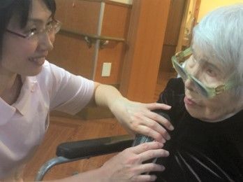 椅子に座ったメガネをかけた白髪の高齢女性の胸に手を伸ばしている女性スタッフ