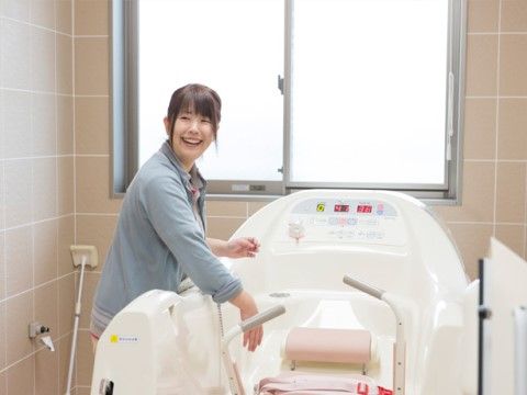 座ったまま入浴する設備の中に手を入れて笑顔で振り向くスタッフ