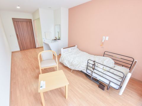 明るい配色の広々としたフローリングの部屋には介護用電動ベッドと椅子とテーブルが置かれ、洗面台が設置されている。