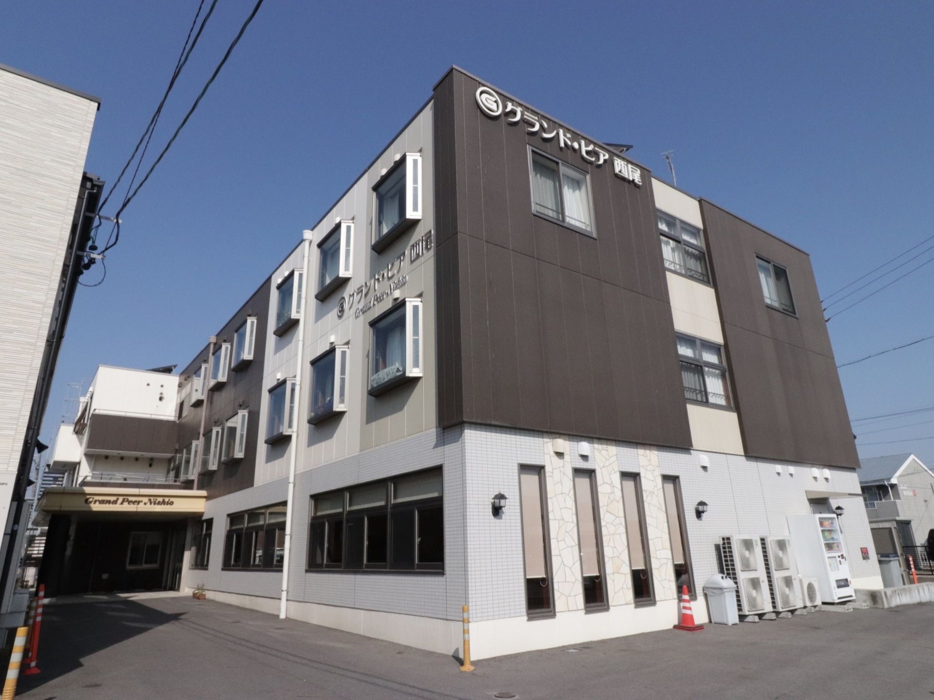 モノトーンカラーがマンションのような見た目の施設外観となっている。スタイリッシュな施設名の看板も特徴的である。