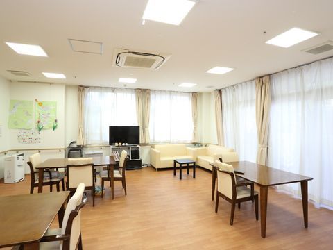 2面に窓があり、クリーム色の床に白い椅子がセットされたテーブルが並ぶ共用スペース