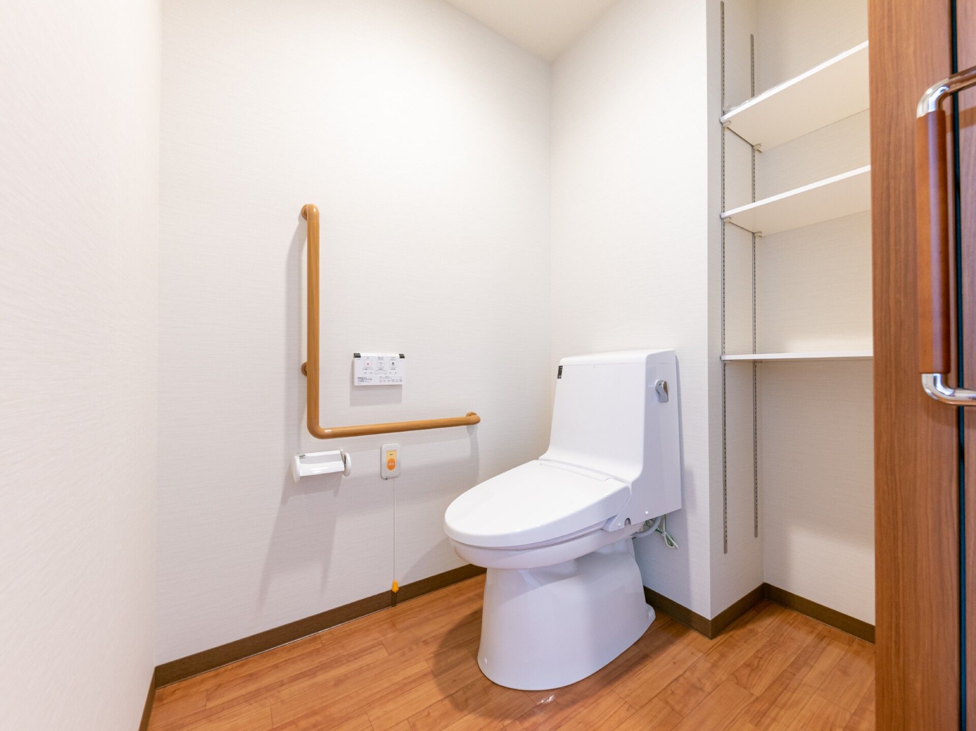 エル字型の手すりやオレンジの呼び出しボタンも付いているトイレは広く、収納棚もある。