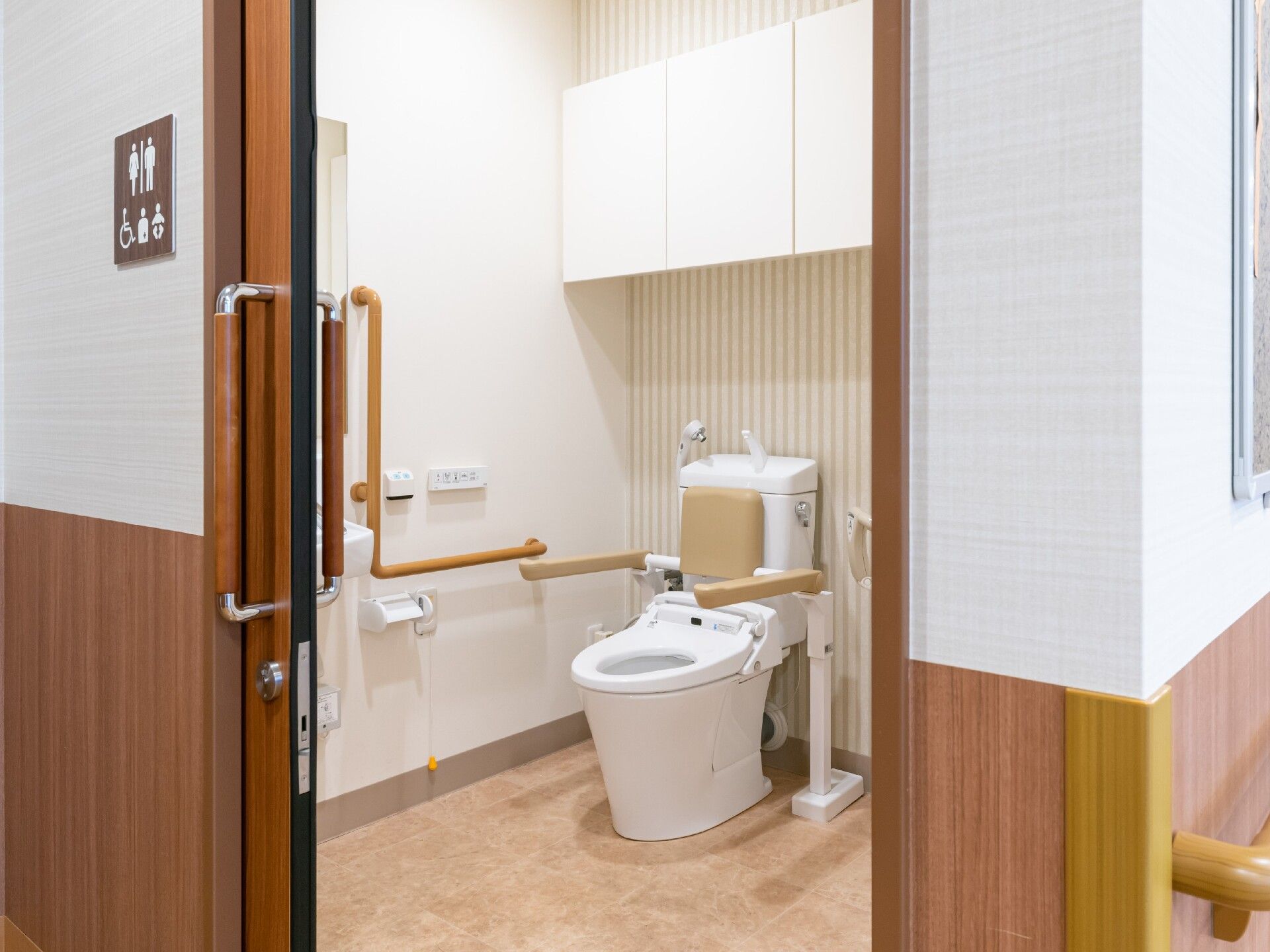 広いトイレには手すりや呼び出しボタンも設置され、便座にも手すりと背もたれがあり、スライドドアが付いている。